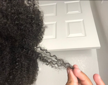 A reviewer with curly hair, holding a strand of it out for inspection