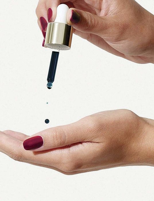 A hand using a dropper to apply the blue serum into the palm.