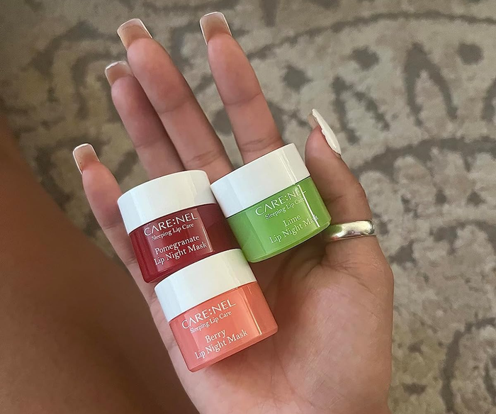 A hand holding two Care:Nel lip masks: berry, pomegranate, and lime flavors.