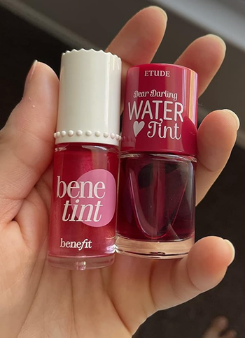 A hand holds two bottles of lip tint: BeneTint by Benefit and Dear Darling Water Tint by Etude