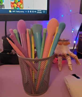 A collection of makeup brushes in various pastel colors, neatly arranged in a cup