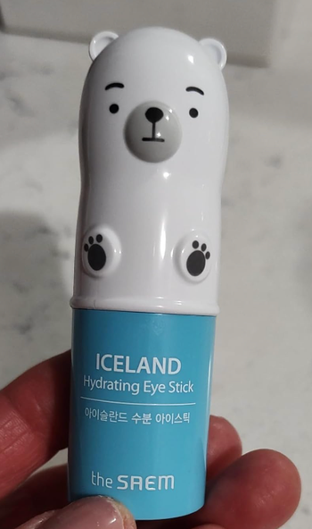 The reviewer holding their blue hydrating stick, topped with a polar bear-shaped cap