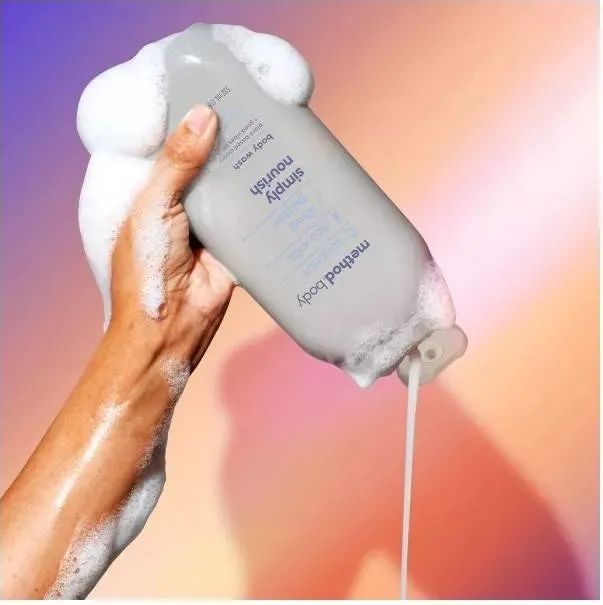A model’s hand holding the Method The Body Wash bottle, with foamy lather highlighting the product's use in action.