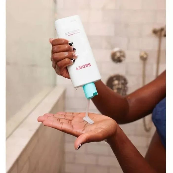 A model dispensing Sadie B conditioner into their palm while in the shower.