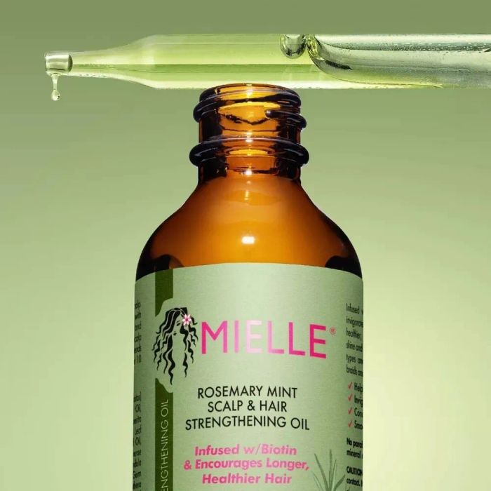 A bottle of Mielle Rosemary Mint Scalp & Hair Strengthening Oil with a dropper dispensing oil, promoted as a solution for healthier, longer hair thanks to biotin.