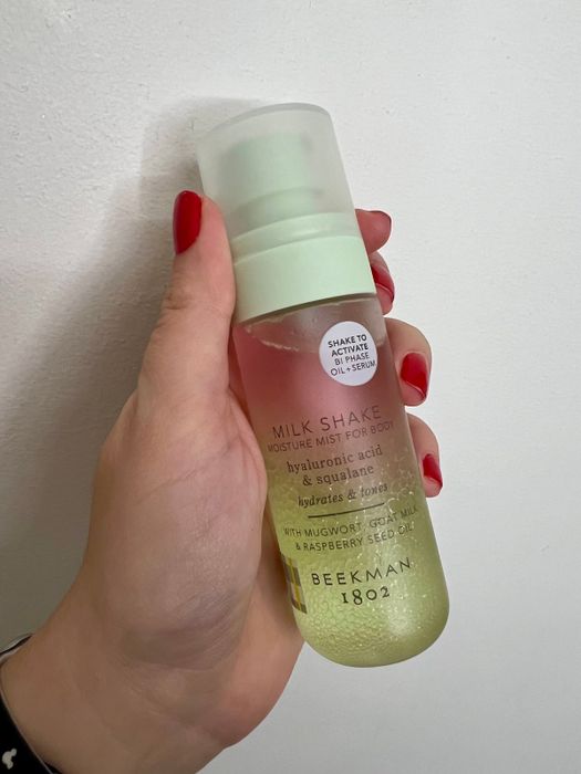 A hand holds a Beekman 1802 Milk Shake Moisture Mist for the body, infused with hyaluronic acid and squalane, a refreshing skincare spray