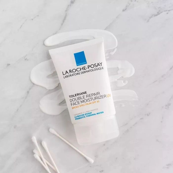 La Roche-Posay Toleriane Double Repair Face Moisturizer with UV SPF 30, presented on a marble surface with swipes of the product and three cotton swabs beside it.