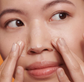 A person applying a nose strip to their face.