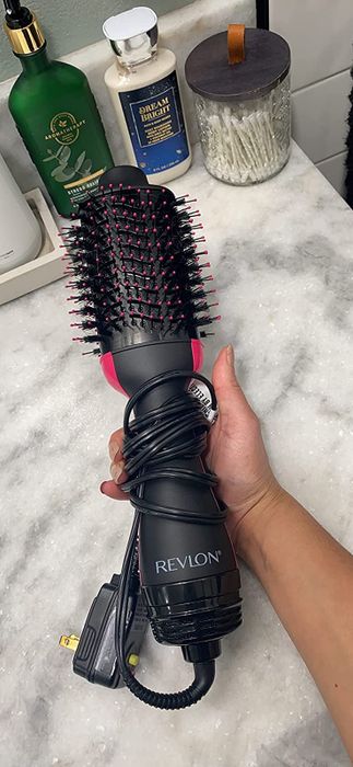 A hand holds the Revlon hair dryer, ready for use.