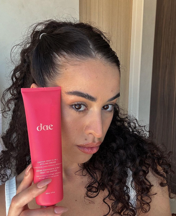 A person holding a pink tube of styling cream.