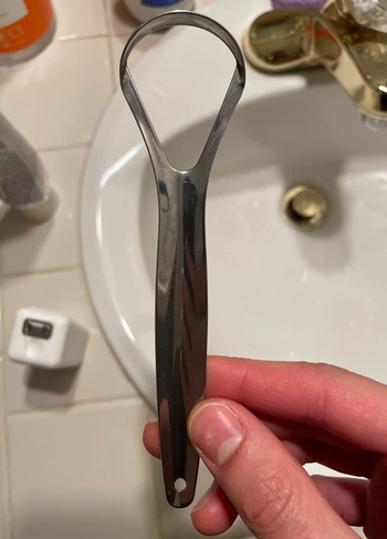 Reviewer holding a steel tongue scraper.