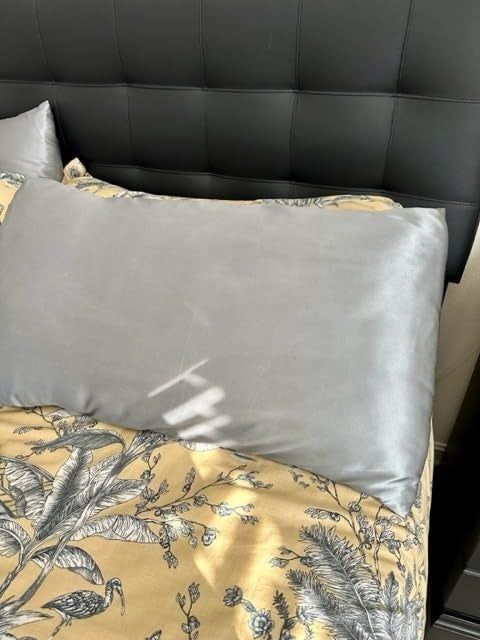 A bed with a black tufted headboard, a silver satin pillowcase, and a duvet cover with a botanical print design.