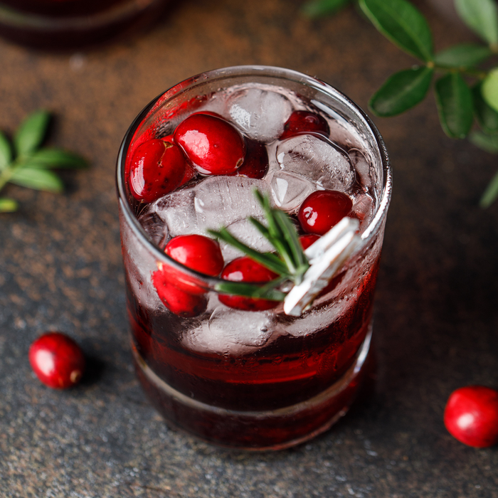 Cranberry cocktail served over ice. A festive Christmas drink with sugar and rosemary garnished glasses