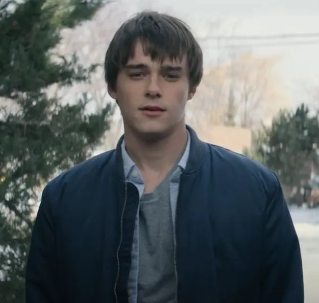 A person standing outdoors, dressed in a casual jacket and shirt, with a reflective or thoughtful look on their face.