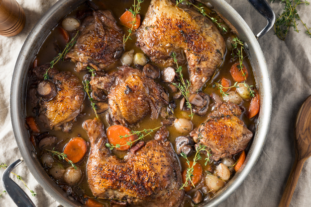 A dish of coq au vin featuring chicken, carrots, mushrooms, pearl onions, and herbs cooked together in a rich red wine sauce