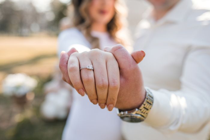A couple holding hands, with the engagement ring clearly visible on the woman's hand, in an outdoor environment