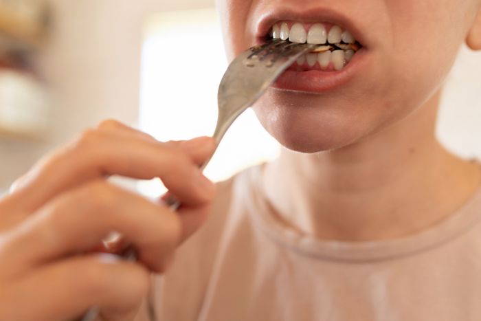 Close-up of a person biting a fork, focusing on their teeth and the utensil.
