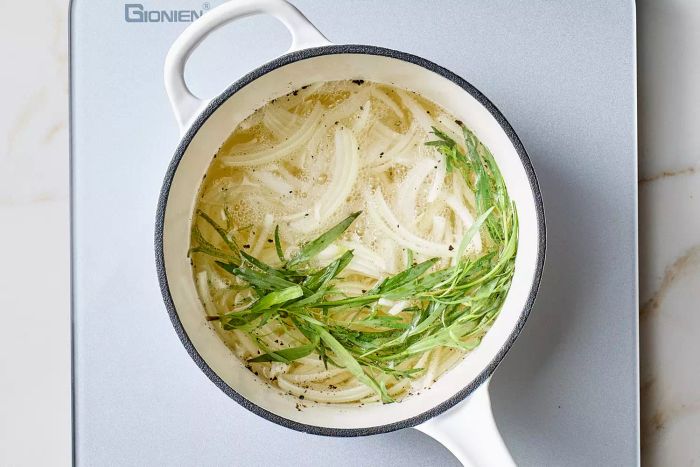 White wine, onion, tarragon, and other ingredients gently simmering together in a pot.