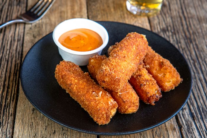 a black plate filled with fried food accompanied by a dipping sauce cup
