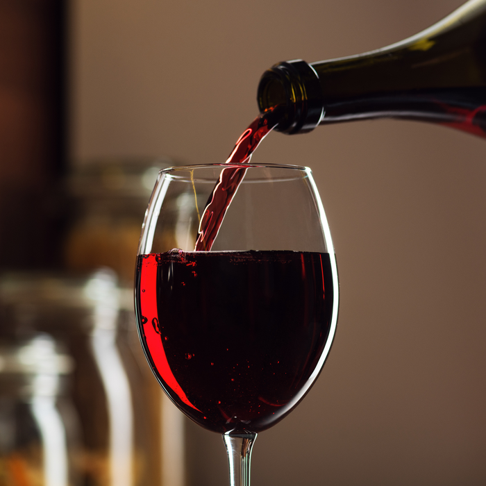 Close-up shot of red wine being poured into a glass, creating bubbles and splashes on a kitchen table with a high-quality studio finish