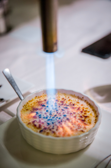 A torch browning sugar atop crème brûlée in a white dish.