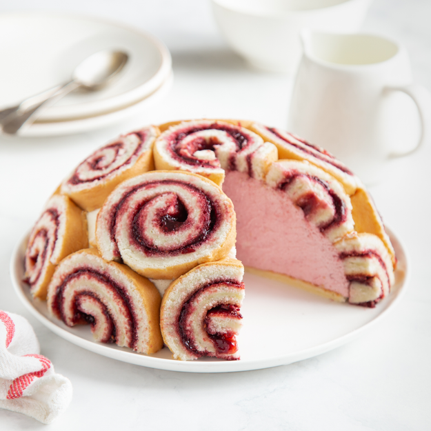 A round-shaped dessert composed of spirals of jam-filled sponge cake, with a cut-out section revealing a pink center