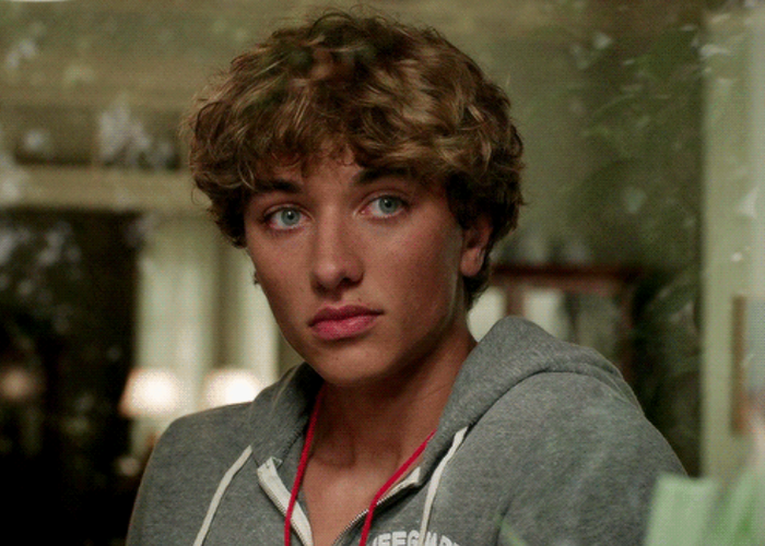 Jeremiah dressed in a cozy hoodie gazes out a window, soft lighting surrounding him in the background