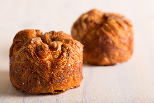 Two golden-brown, crispy kouign-amann pastries with layers of caramelized sugar, placed on a neutral background