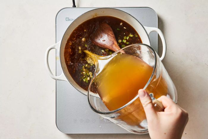 Pouring broth into the pot with scallions and other aromatics