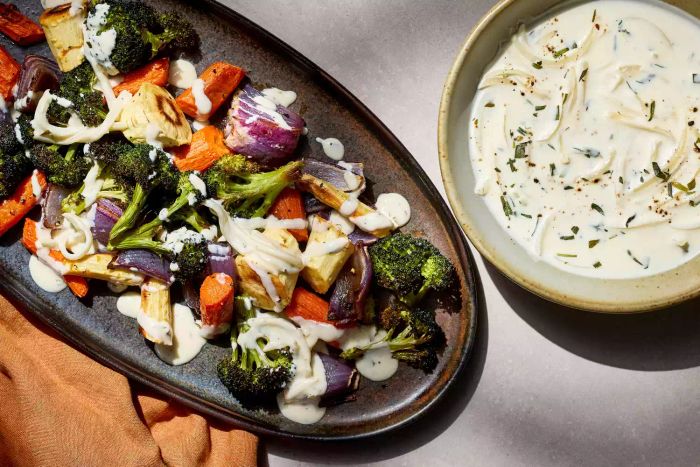 A bowl of tarragon cream sauce next to a platter of freshly roasted vegetables.