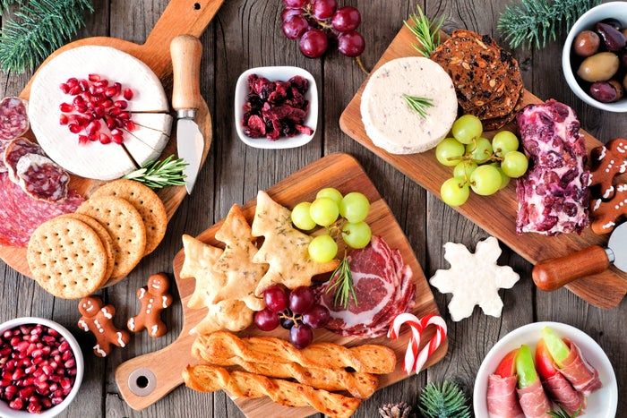 A holiday-inspired charcuterie board featuring an assortment of cured meats, artisan cheeses, crisp crackers, fresh fruits, and festive cookies beautifully arranged on wooden platters