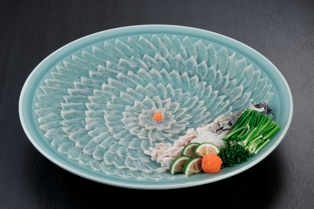 Delicately arranged slices of sashimi on a large platter, garnished with lime wedges, fresh chives, and a hint of orange roe