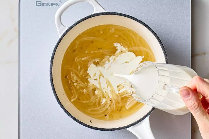 Pouring the cream into the pot with the simmering onion and wine mixture.