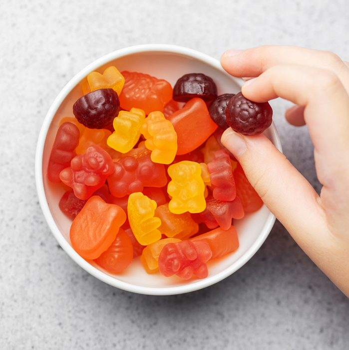 Chewable gummy bear vitamins and supplements. A girl holds a gummy bear vitamin in her hands.