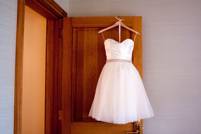 A short white dress with a strapless bodice and a silver beaded waistband, hanging on a wooden door