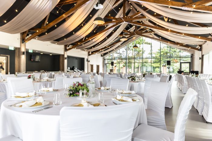 A sophisticated wedding reception arrangement featuring a draped ceiling, round tables with white linens, and floral centerpieces in a bright, airy space