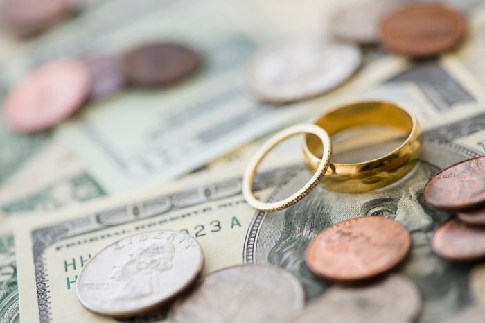 Gold wedding rings placed atop a stack of cash and coins, symbolizing the expensive nature of weddings