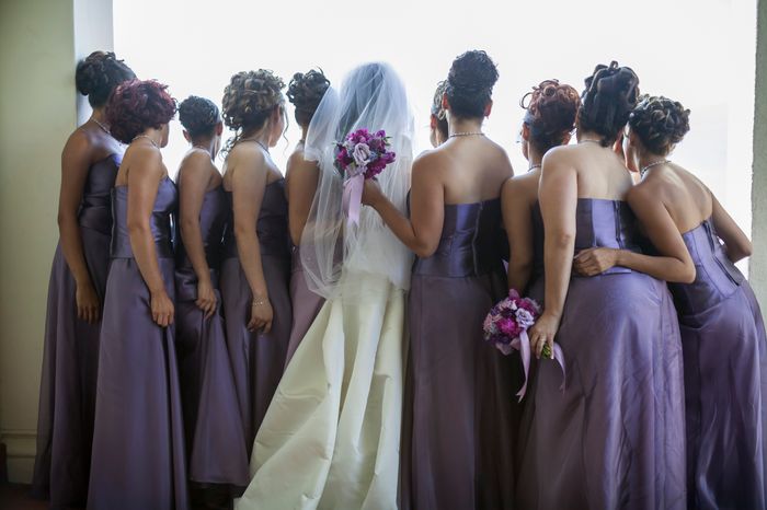 A bride in her gown with bridesmaids in sophisticated dresses, holding bouquets, gazing out a window