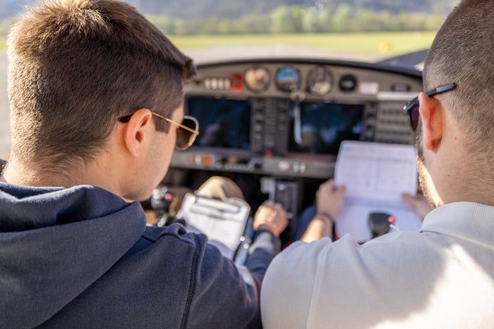 Two people in a cockpit, one holding a checklist