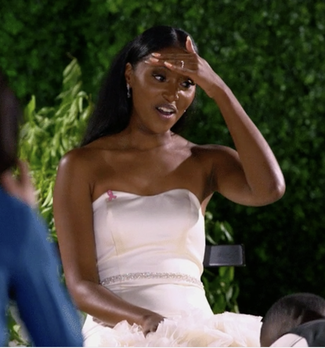 A bride in a strapless, white wedding dress, visibly stunned, with her hand on her forehead