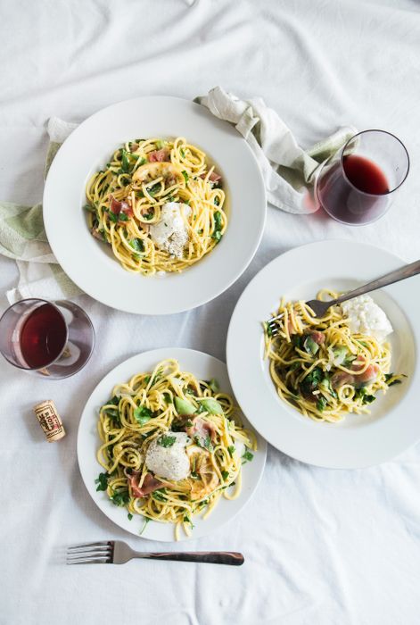 Three white round plates of pasta beside two glass cups