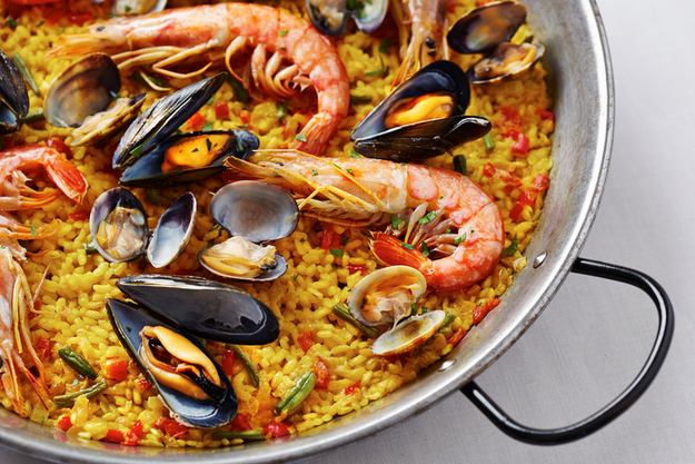 A pan filled with seafood paella, featuring shrimp, mussels, and clams served on a bed of saffron rice.