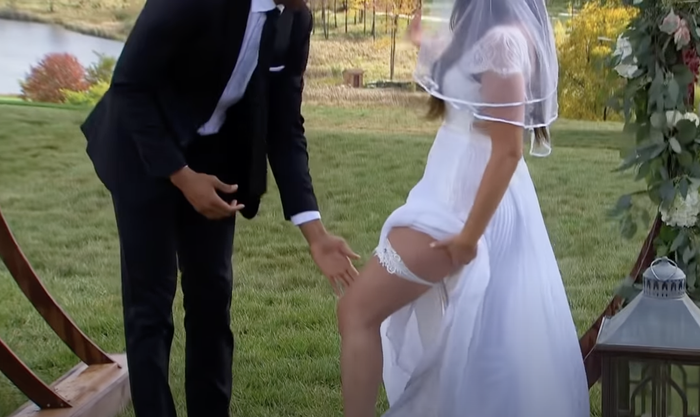 A close-up of a groom reaching for the garter on the bride’s leg