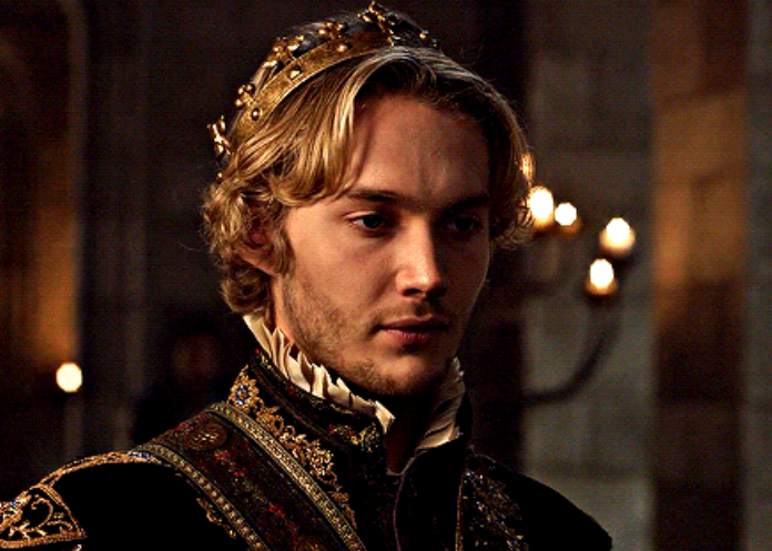 A man dressed in an intricate period costume with a crown, bathed in dim lighting