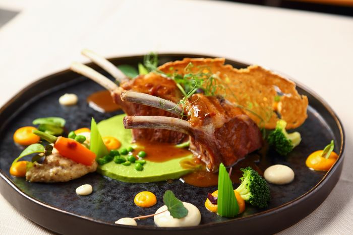 Gourmet dish featuring lamb chops, vibrant vegetables, creamy puree, and a decorative crisp on a dark plate