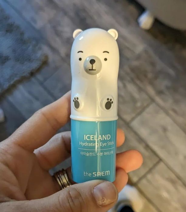 A reviewer holding their blue hydrating stick, which has an adorable polar bear-shaped cap on top.
