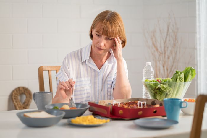 A person sitting at a table with a variety of dishes, including salad, pizza, and eggs, looking thoughtful or concerned.
