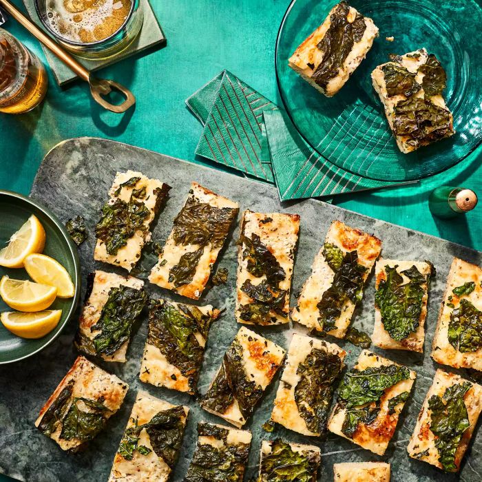 Kale flatbread bites on a gray serving tray with lemon wedges in a bowl