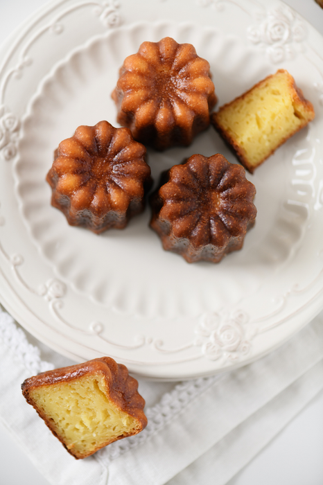 A plate featuring five cannelés, the classic French pastry with a crispy caramelized exterior and soft, custardy interior