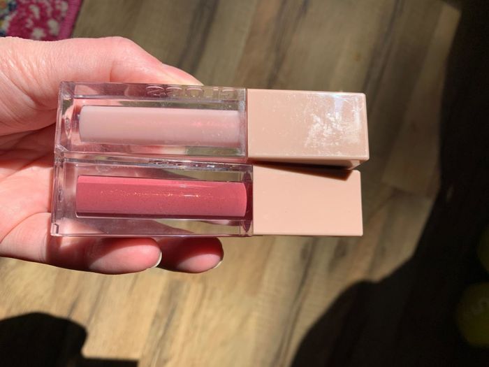A reviewer holding two bottles of lip gloss.